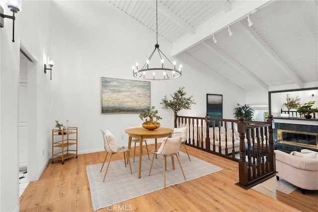 dining space featuring beam ceiling, light hardwood / wood-style floors, high vaulted ceiling, and a notable chandelier