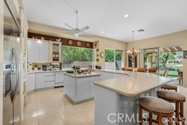 kitchen with white cabinetry, a center island, decorative light fixtures, light tile patterned floors, and ceiling fan with notable chandelier