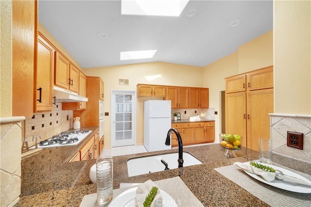 kitchen featuring white appliances, backsplash, lofted ceiling with skylight, sink, and kitchen peninsula