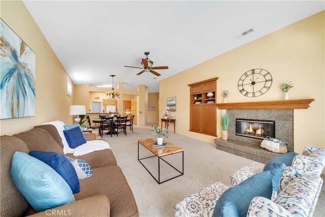 living room featuring a high end fireplace, light carpet, and ceiling fan with notable chandelier