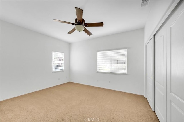 unfurnished bedroom featuring light carpet, a closet, multiple windows, and ceiling fan