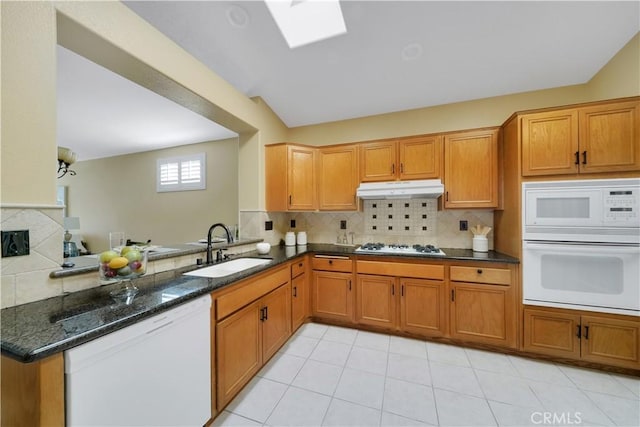 kitchen with kitchen peninsula, white appliances, dark stone counters, and sink