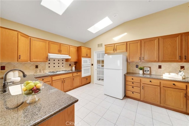 kitchen with light stone countertops, backsplash, white appliances, sink, and light tile patterned floors