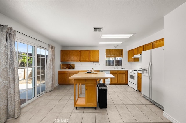 kitchen featuring white appliances, sink, a skylight, light tile patterned floors, and a kitchen island