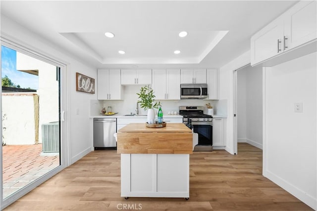 kitchen with white cabinets, light hardwood / wood-style floors, a raised ceiling, and appliances with stainless steel finishes