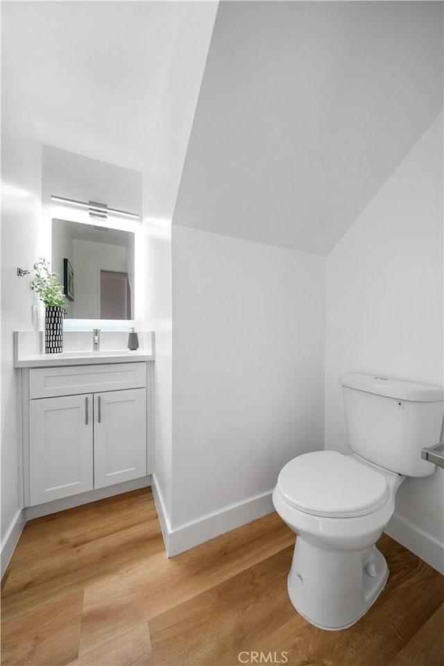 bathroom featuring hardwood / wood-style flooring, vanity, toilet, and vaulted ceiling