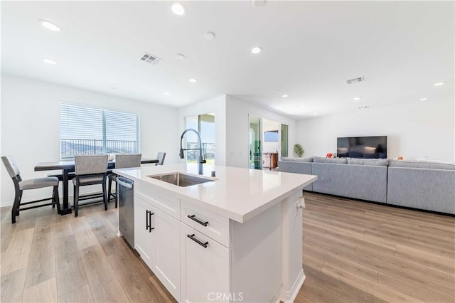 kitchen with stainless steel dishwasher, a kitchen island with sink, sink, light hardwood / wood-style floors, and white cabinetry