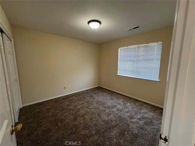 unfurnished bedroom with a closet, a textured ceiling, and dark colored carpet