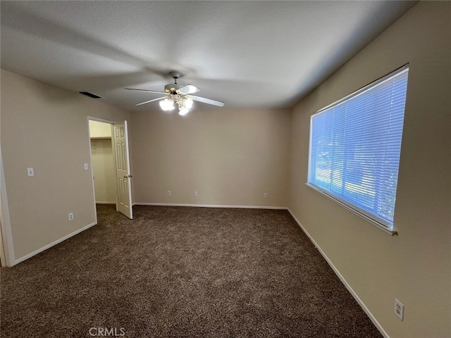 empty room featuring ceiling fan and dark carpet