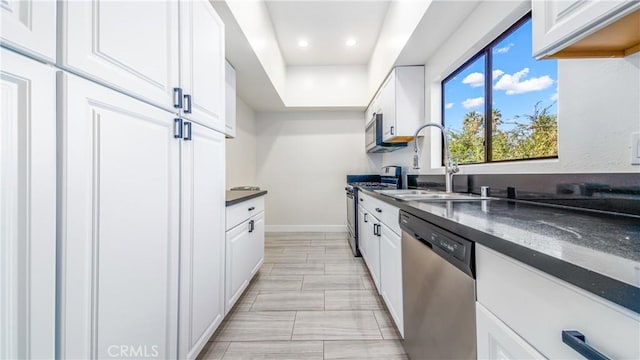 kitchen with white cabinets, stainless steel appliances, dark stone counters, and sink