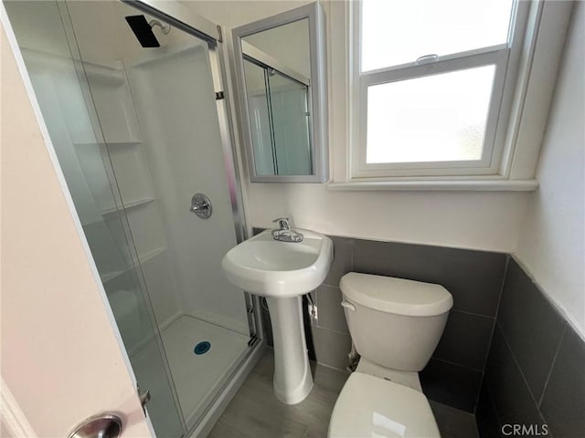 bathroom with a shower with door, toilet, and tile walls