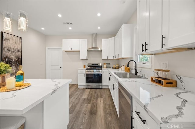 kitchen featuring appliances with stainless steel finishes, hanging light fixtures, wall chimney exhaust hood, white cabinets, and sink