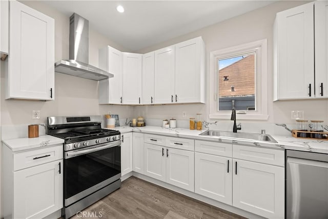 kitchen featuring hardwood / wood-style flooring, stainless steel appliances, wall chimney range hood, white cabinets, and sink