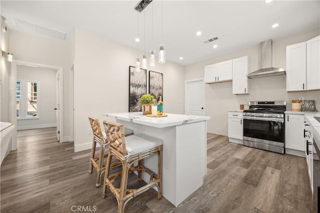 kitchen with stainless steel gas stove, wall chimney range hood, white cabinetry, and a kitchen island