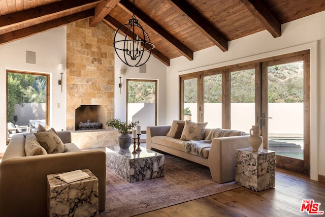 living room featuring a tiled fireplace, hardwood / wood-style floors, beamed ceiling, and an inviting chandelier