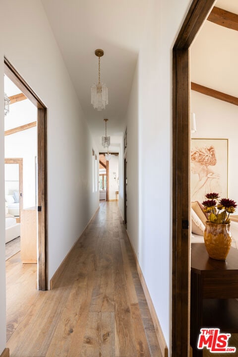 hall with lofted ceiling with beams, wood-type flooring, and an inviting chandelier