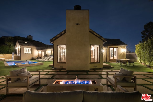 back house at night with french doors, a patio, and an outdoor living space with a fire pit