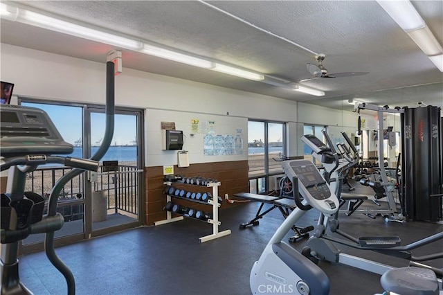 workout area with a textured ceiling, a water view, and ceiling fan