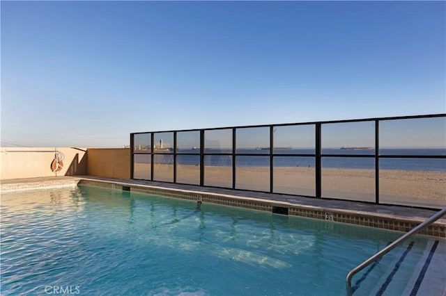 view of swimming pool with a water view and a view of the beach