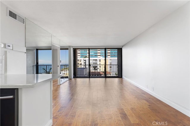 unfurnished living room with wood-type flooring, a wall of windows, and a wealth of natural light