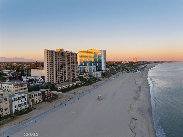 aerial view at dusk featuring a water view and a beach view