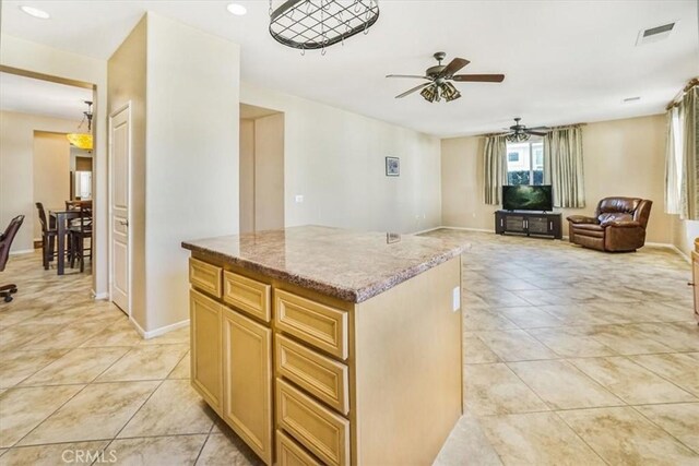 kitchen with light stone counters, ceiling fan, light brown cabinets, light tile patterned floors, and a kitchen island