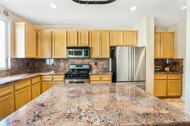 kitchen with sink, light stone counters, tasteful backsplash, light brown cabinets, and appliances with stainless steel finishes