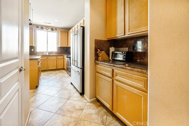 kitchen with tasteful backsplash, light brown cabinetry, light tile patterned floors, and stainless steel appliances