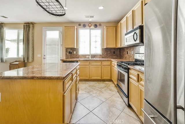 kitchen featuring appliances with stainless steel finishes, a center island, tasteful backsplash, light stone countertops, and light brown cabinets