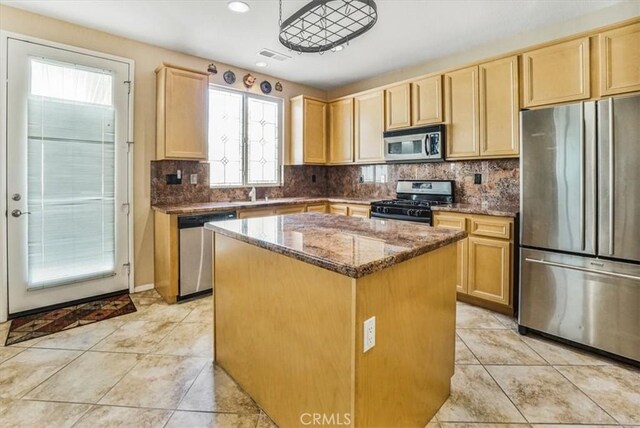 kitchen with stainless steel appliances, light tile patterned floors, dark stone countertops, light brown cabinetry, and a kitchen island