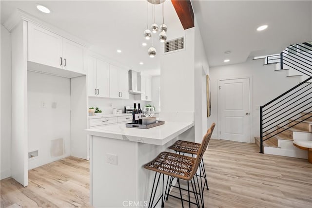 kitchen featuring decorative light fixtures, light hardwood / wood-style floors, white cabinetry, and kitchen peninsula