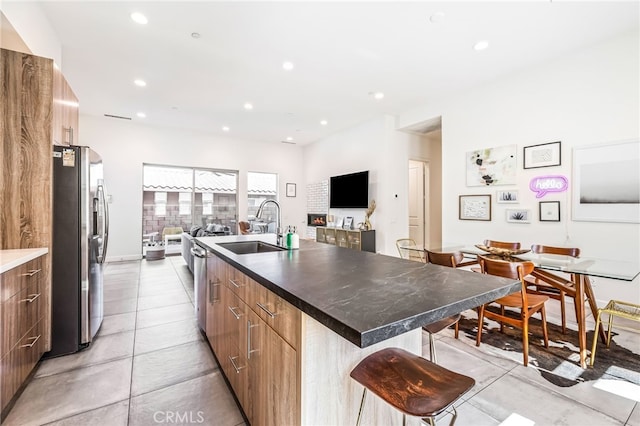 kitchen with sink, stainless steel refrigerator with ice dispenser, a breakfast bar area, a kitchen island with sink, and light tile patterned flooring