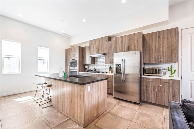 kitchen with appliances with stainless steel finishes, tasteful backsplash, a kitchen island with sink, sink, and light tile patterned floors