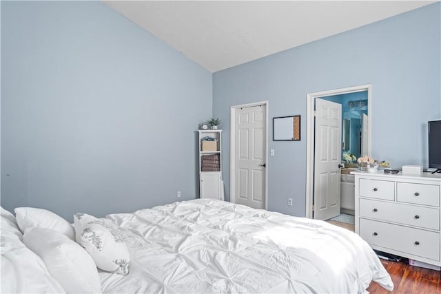 bedroom with connected bathroom, dark wood-type flooring, and vaulted ceiling