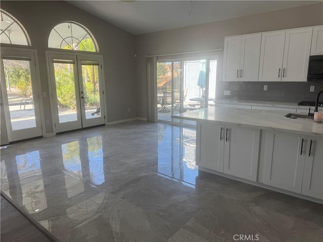 kitchen with light stone countertops, white cabinetry, sink, and tasteful backsplash