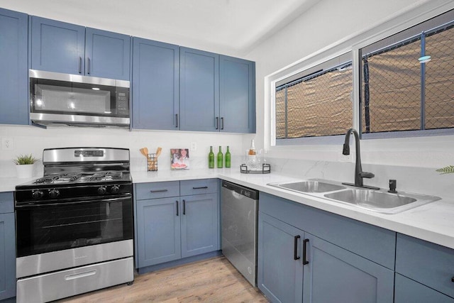 kitchen featuring blue cabinets, sink, light stone countertops, light wood-type flooring, and stainless steel appliances