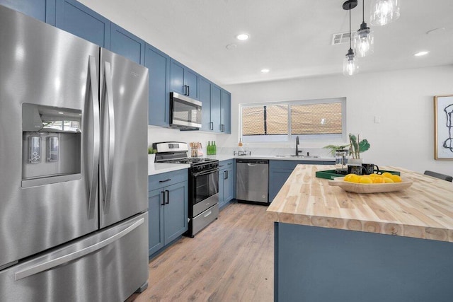 kitchen featuring wood counters, appliances with stainless steel finishes, blue cabinets, decorative light fixtures, and light hardwood / wood-style flooring