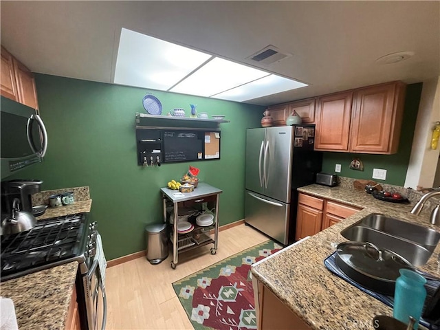 kitchen featuring light stone countertops, sink, appliances with stainless steel finishes, and light hardwood / wood-style flooring