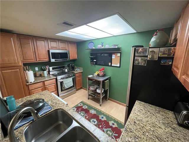 kitchen featuring light stone counters, sink, stainless steel appliances, and light hardwood / wood-style floors