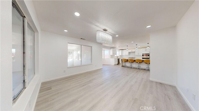 unfurnished living room with light wood-type flooring and an inviting chandelier