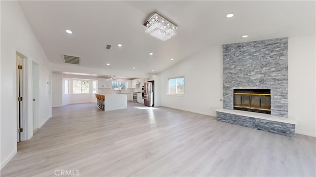 unfurnished living room featuring a fireplace, an inviting chandelier, high vaulted ceiling, and light wood-type flooring