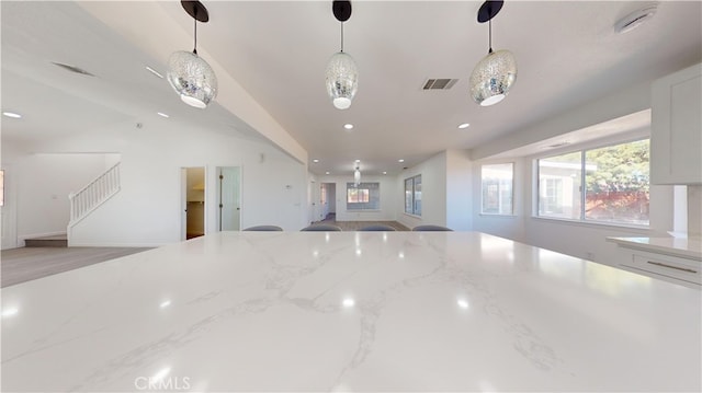 kitchen with white cabinets, decorative light fixtures, light stone counters, and lofted ceiling