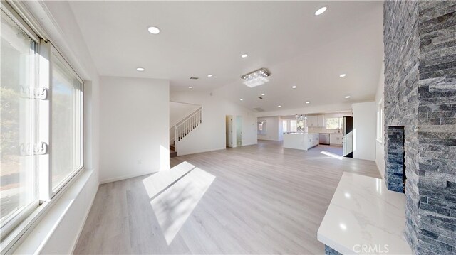 living room with vaulted ceiling, light hardwood / wood-style floors, and a stone fireplace