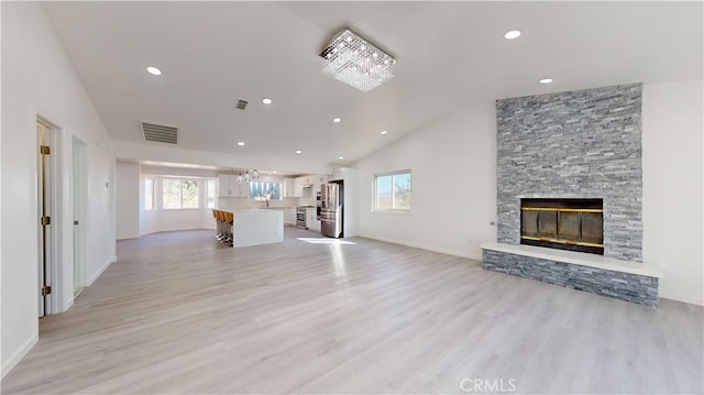 unfurnished living room featuring a fireplace, light hardwood / wood-style flooring, high vaulted ceiling, and an inviting chandelier