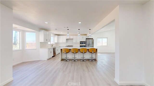 kitchen with a center island, light hardwood / wood-style floors, pendant lighting, white cabinets, and appliances with stainless steel finishes