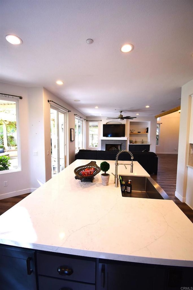 kitchen with light stone countertops, dark hardwood / wood-style flooring, ceiling fan, and a center island with sink