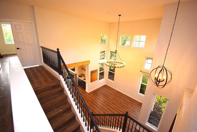 stairs with wood-type flooring, a high ceiling, and an inviting chandelier