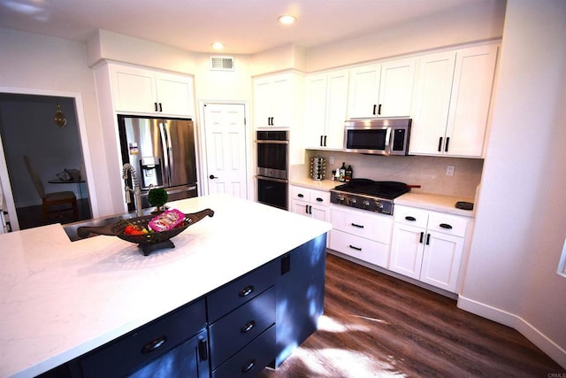 kitchen featuring light stone countertops, appliances with stainless steel finishes, tasteful backsplash, dark hardwood / wood-style flooring, and white cabinetry