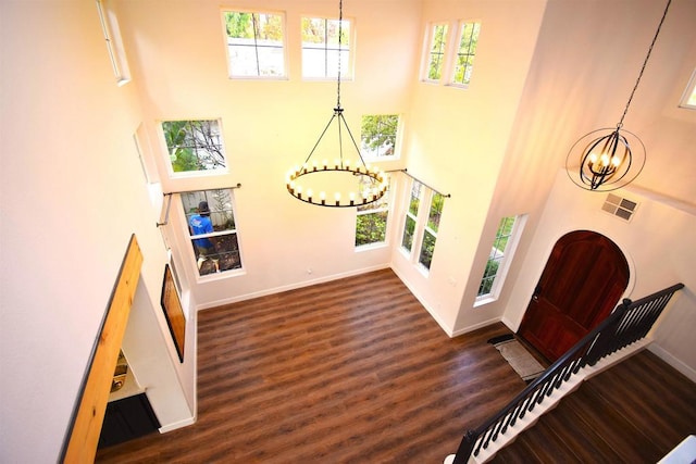 entryway with a towering ceiling, dark wood-type flooring, a wealth of natural light, and an inviting chandelier