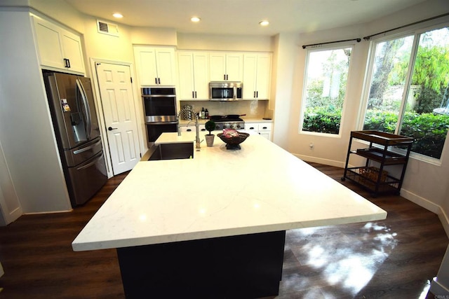 kitchen featuring appliances with stainless steel finishes, light stone counters, a kitchen island with sink, sink, and white cabinets